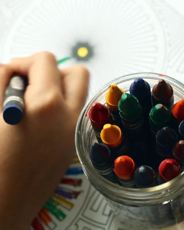 Child coloring with a jar of crayons