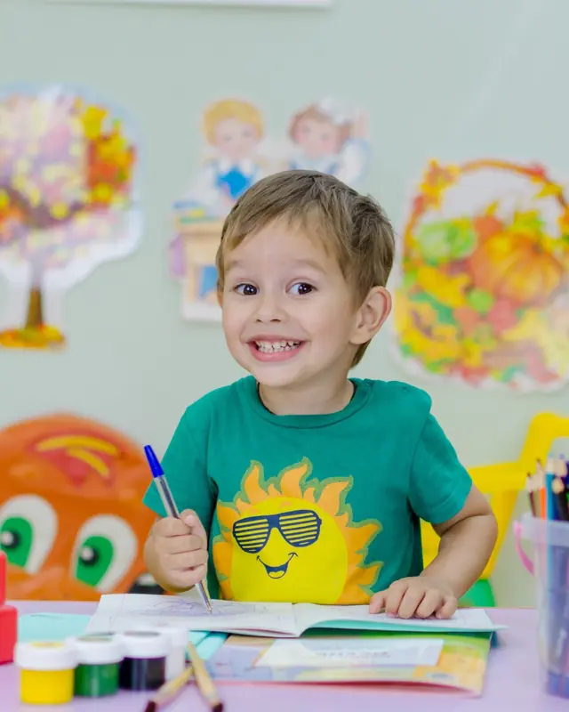 Smiling preschooler drawing at a desk with a globe and colored pencils